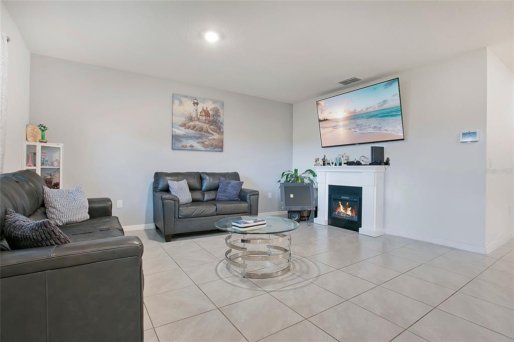 A living room features gray leather sofas, a glass coffee table, and a wall-mounted fireplace — 3676 SCARLET OAK DRIVE, ST CLOUD, FL