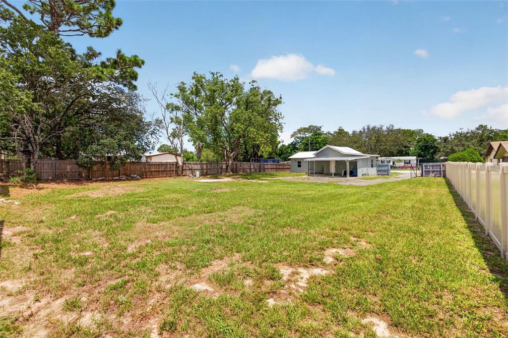 A large, grassy backyard features a wooden fence, mature trees, and a detached garage — 6462 SEALAWN DRIVE, SPRING HILL, FL