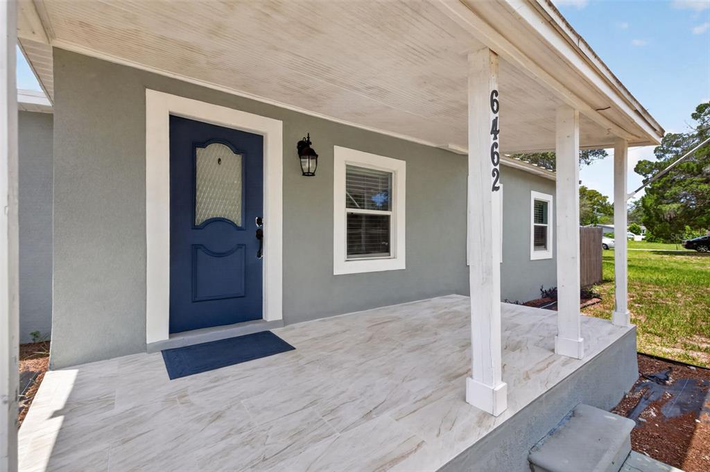 The exterior of a house features a covered porch with tiled flooring and a blue door — 6462 SEALAWN DRIVE, SPRING HILL, FL