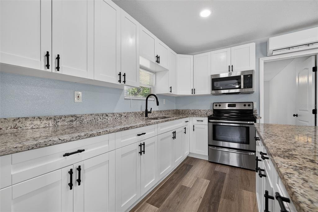 A kitchen features white cabinets, granite countertops, stainless steel appliances, and wood-look flooring — 6462 SEALAWN DRIVE, SPRING HILL, FL