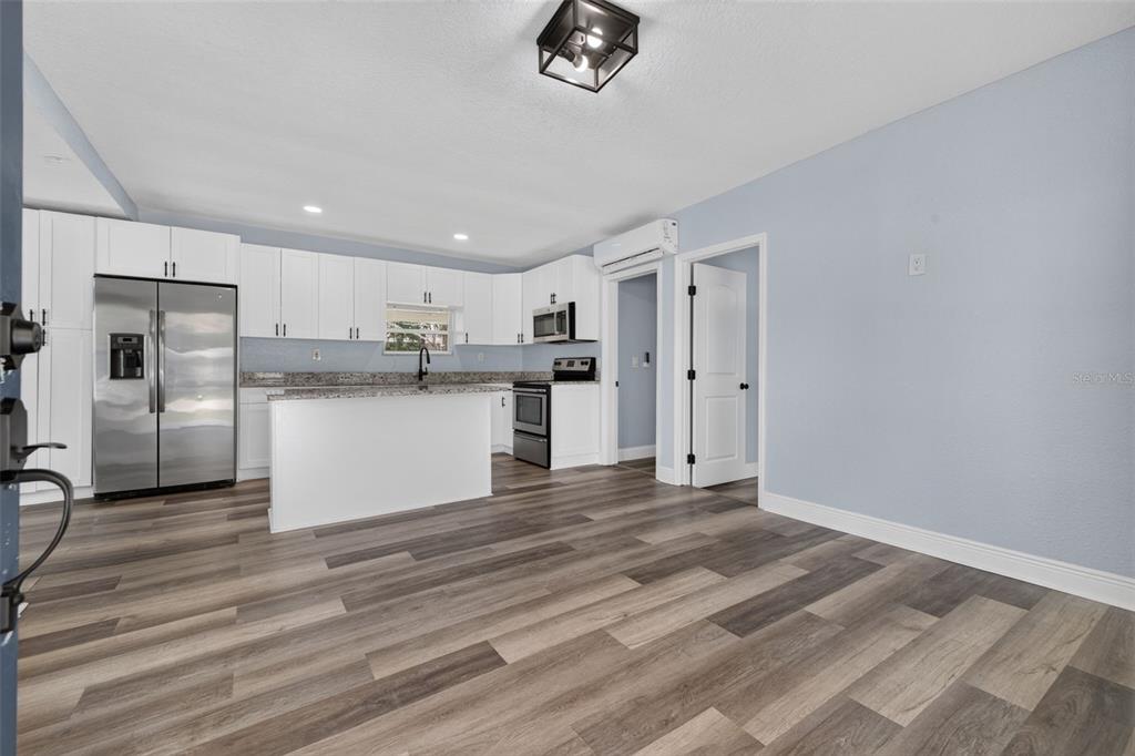 A kitchen with white cabinets, stainless steel appliances, and an island opens to a room — 6462 SEALAWN DRIVE, SPRING HILL, FL