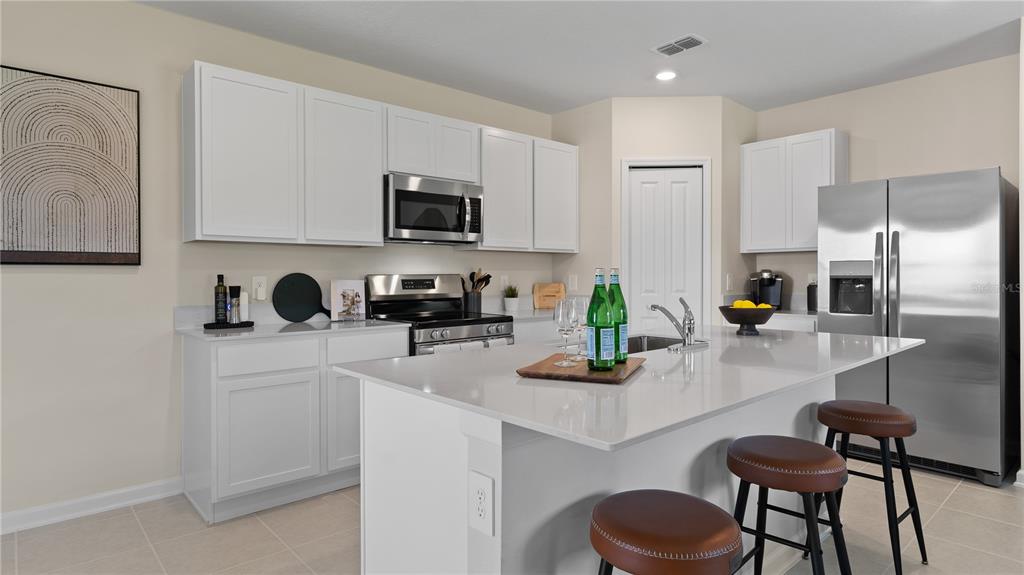 A modern kitchen features white cabinets, stainless steel appliances, a quartz island, and bar stools — 1564 WILLOW GARDEN LOOP, EUSTIS, FL