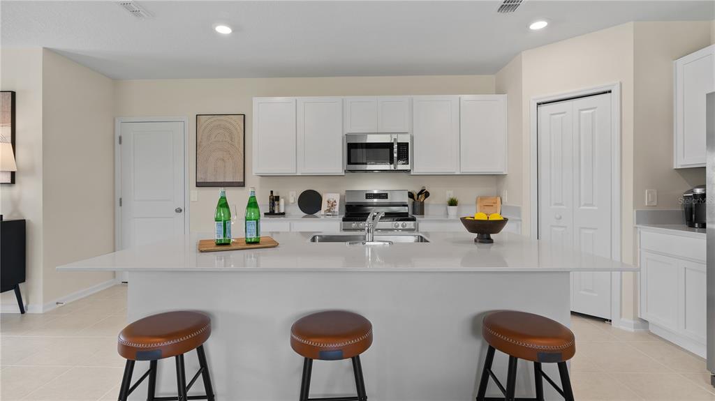 A modern kitchen features white cabinets, a large island with three stools, and stainless appliances — 1564 WILLOW GARDEN LOOP, EUSTIS, FL