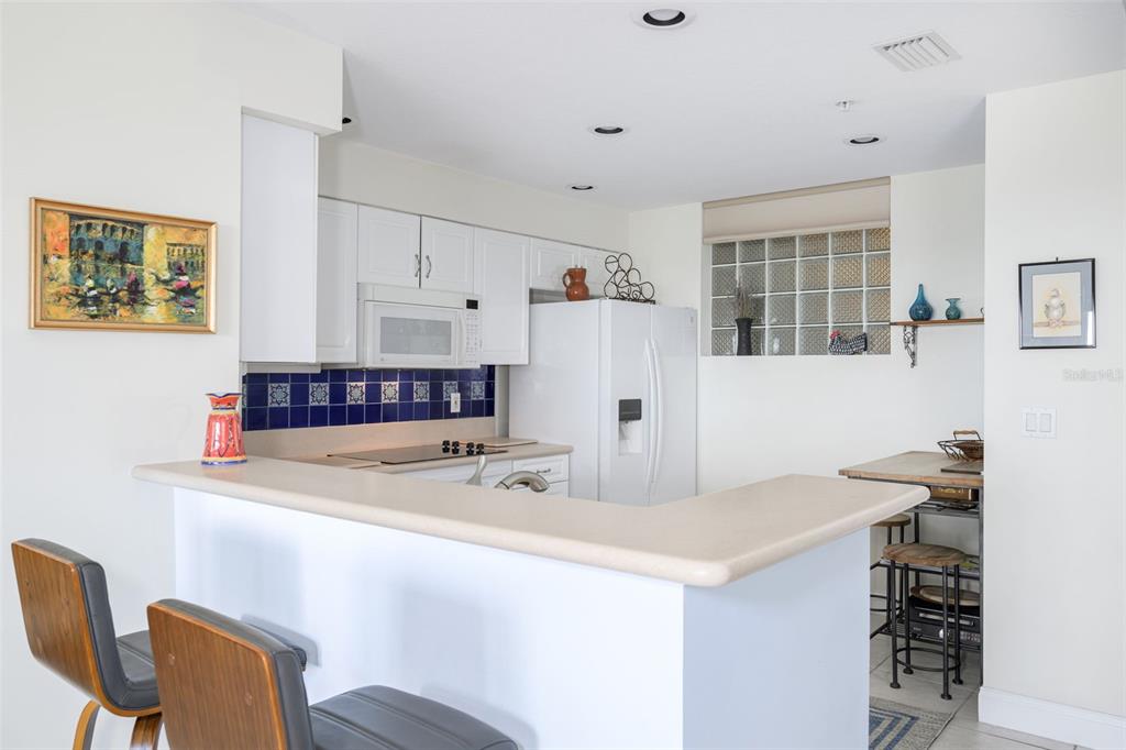 A kitchen with white cabinets and a breakfast bar opens to an entryway with a door — 4624 HARBOUR VILLAGE BOULEVARD UNIT 4504, PONCE INLET, FL