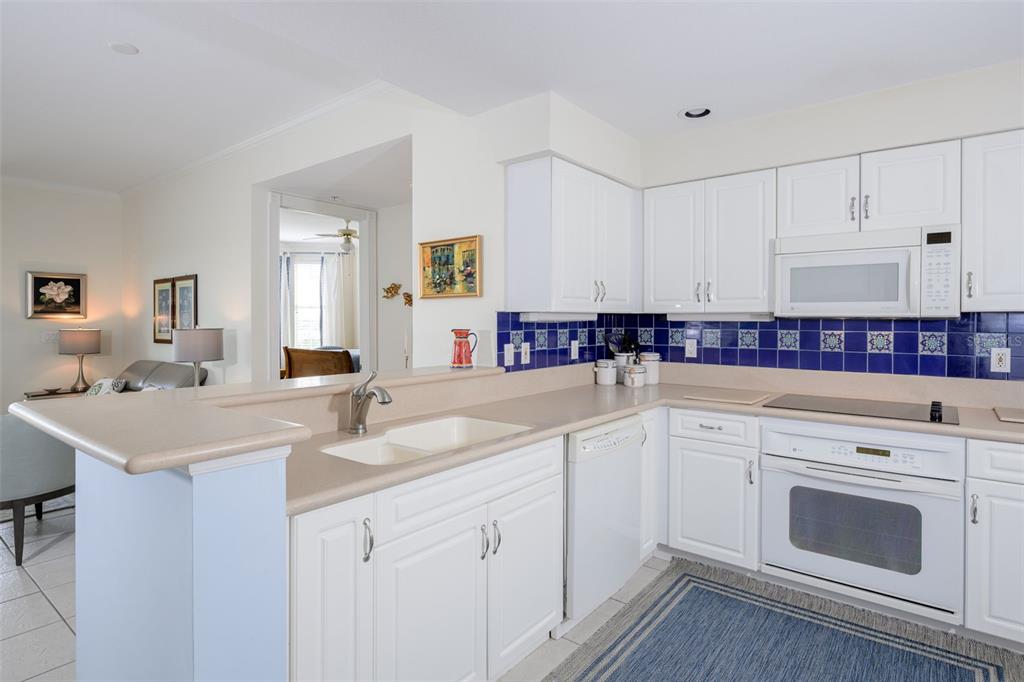 A kitchen with white cabinets, blue tile backsplash, beige countertops, and white appliances — 4624 HARBOUR VILLAGE BOULEVARD UNIT 4504, PONCE INLET, FL