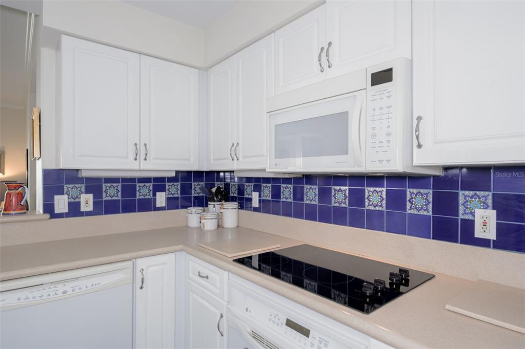 A kitchen with white cabinets and blue tile backsplash opens to a living area and balcony — 4624 HARBOUR VILLAGE BOULEVARD UNIT 4504, PONCE INLET, FL