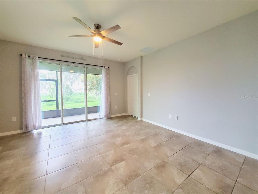 An empty living room features tile flooring, a ceiling fan, and sliding glass doors — 31457 MANGO FADE WAY, SAN ANTONIO, FL