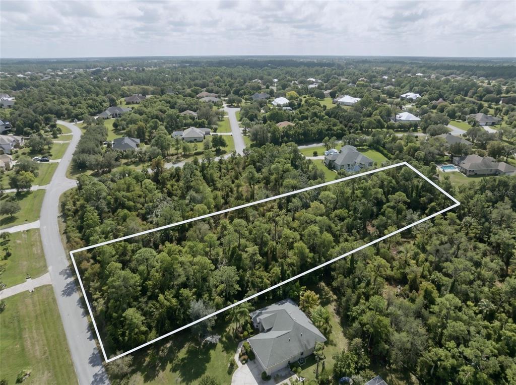 An aerial view shows a rectangular, wooded vacant lot outlined in white within a neighborhood — 5690 CYPRESS CREEK DRIVE, GRANT VALKARIA, FL