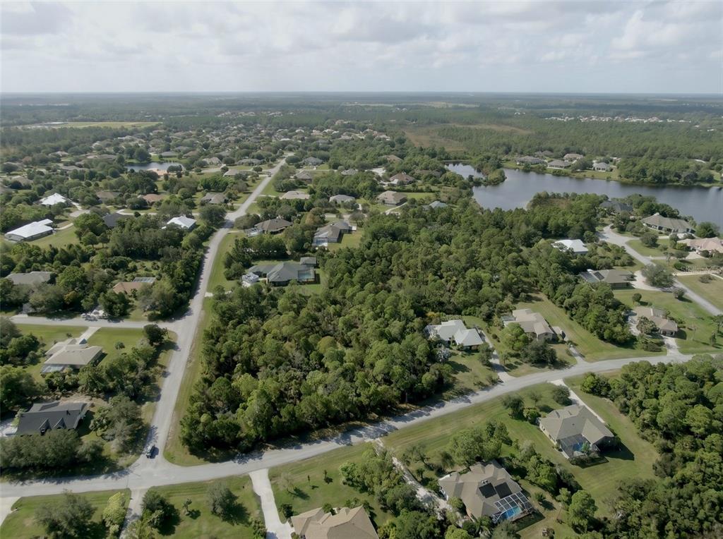 An aerial view shows a suburban neighborhood with houses, dense trees, and a small lake — 5690 CYPRESS CREEK DRIVE, GRANT VALKARIA, FL