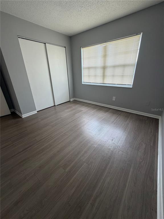 An empty bedroom features gray walls, wood-look flooring, a sliding closet, and a window with blinds — 709 OCEANSIDE CIRCLE UNIT 739, RUSKIN, FL