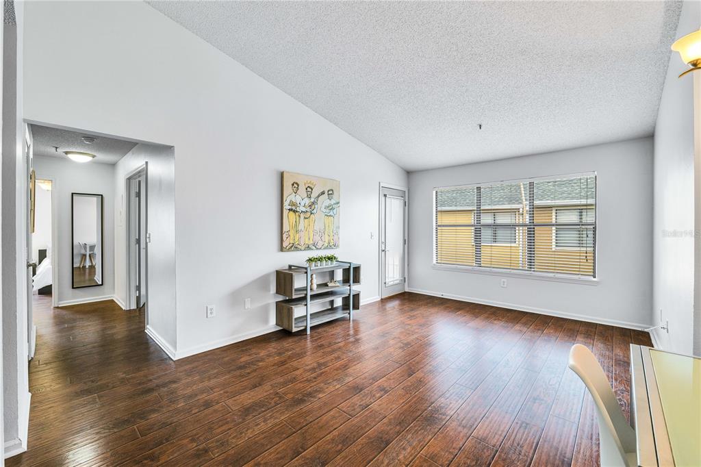A living room with wood-look flooring, a white wall, a window, and a small shelf — 11901 4TH STREET N UNIT 9302, ST PETERSBURG, FL