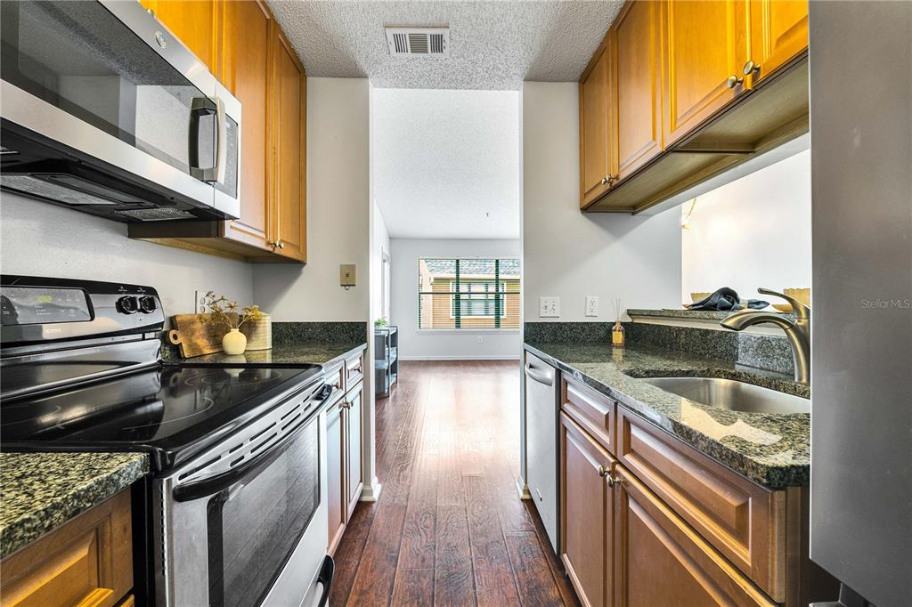 A galley kitchen features wood cabinets, dark granite countertops, and stainless steel appliances — 11901 4TH STREET N UNIT 9302, ST PETERSBURG, FL