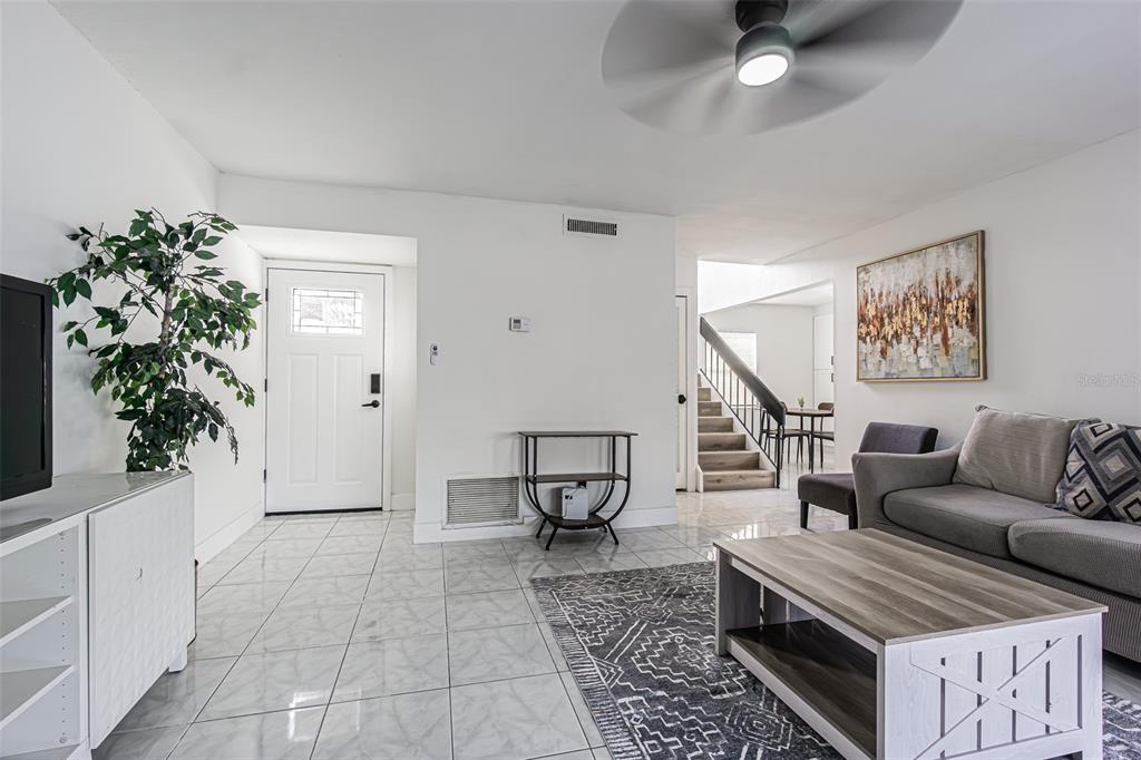 A living room features white tile floors, a grey sofa, and stairs in the background — 10305 BRAMBLEWOOD PLACE, TAMPA, FL