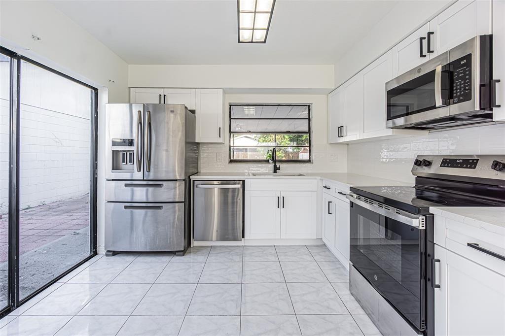 A kitchen with white cabinets, stainless steel appliances, tile flooring, and a sliding glass door — 10305 BRAMBLEWOOD PLACE, TAMPA, FL