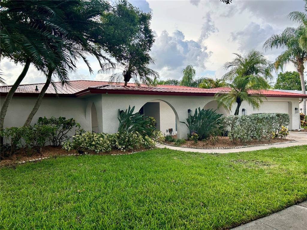 A single-story house with a red metal roof, arched entryways, and palm trees in front — 2126 EGRET DRIVE, CLEARWATER, FL