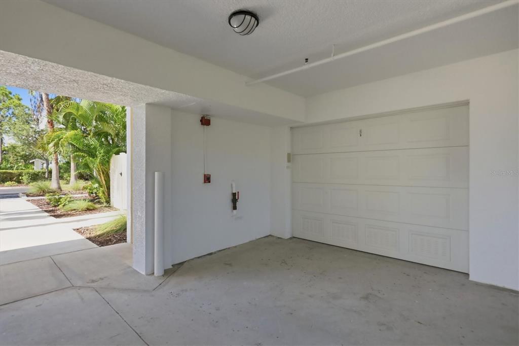 A covered carport features a white garage door, concrete flooring, and a view of palm trees — 8409 PLACIDA ROAD UNIT 308, PLACIDA, FL