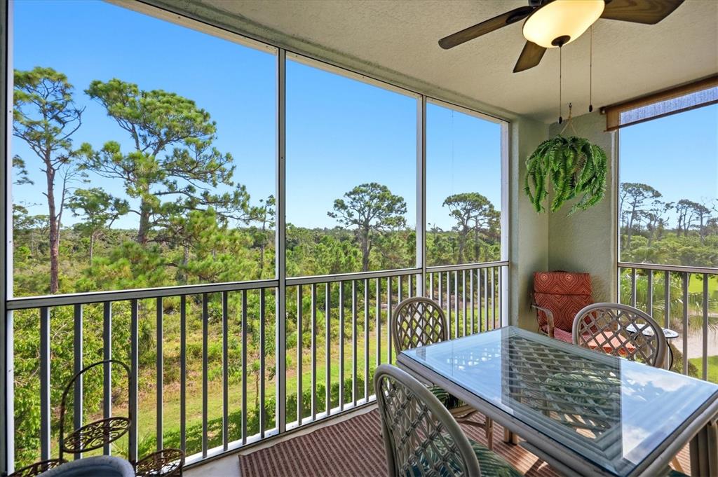 A screened-in balcony features a glass-top dining table, ceiling fan, and views of pine trees — 8409 PLACIDA ROAD UNIT 308, PLACIDA, FL