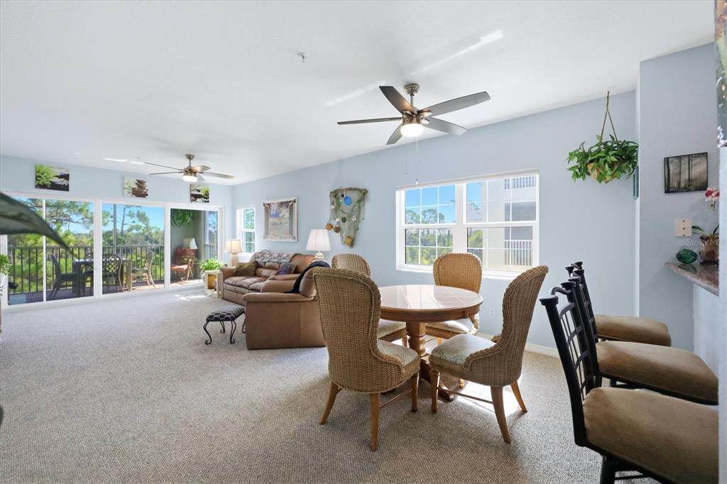 An open-concept living and dining area with light blue walls, carpeted floors, and a balcony — 8409 PLACIDA ROAD UNIT 308, PLACIDA, FL
