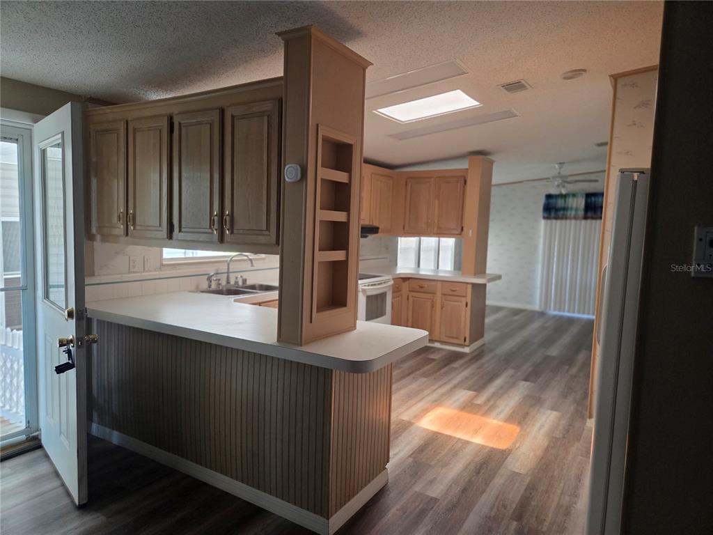 A kitchen with light wood cabinets, white countertops, and wood-look flooring opens to a living area — 3224 MANATEE ROAD, TAVARES, FL
