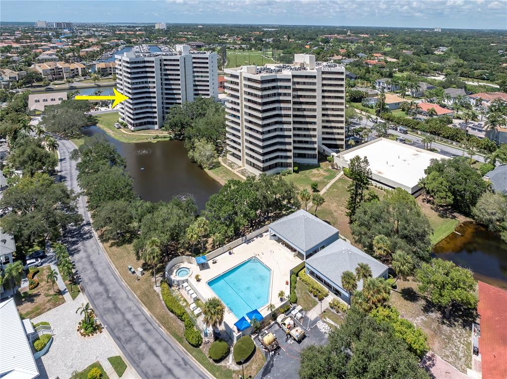 An aerial view shows two high-rise apartment buildings, a swimming pool, and a small lake — 5950 PELICAN BAY PLAZA S UNIT 601, GULFPORT, FL