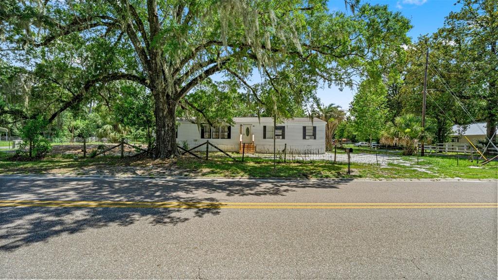 A single-story mobile home sits behind a wooden fence under a large oak tree — 10530 PROSPECT AVENUE, HAMPTON, FL