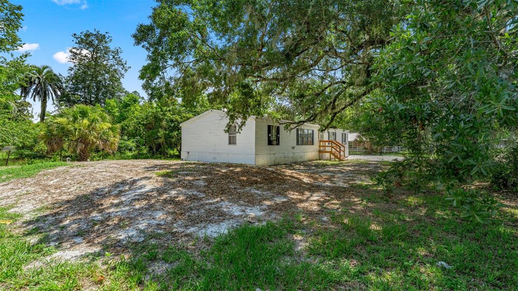 A white mobile home sits on a sandy lot shaded by large, moss-covered oak trees — 10530 PROSPECT AVENUE, HAMPTON, FL