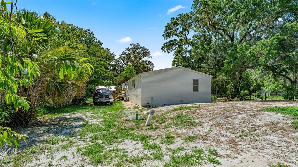 A white mobile home sits on a sandy lot surrounded by trees and a parked truck — 10530 PROSPECT AVENUE, HAMPTON, FL