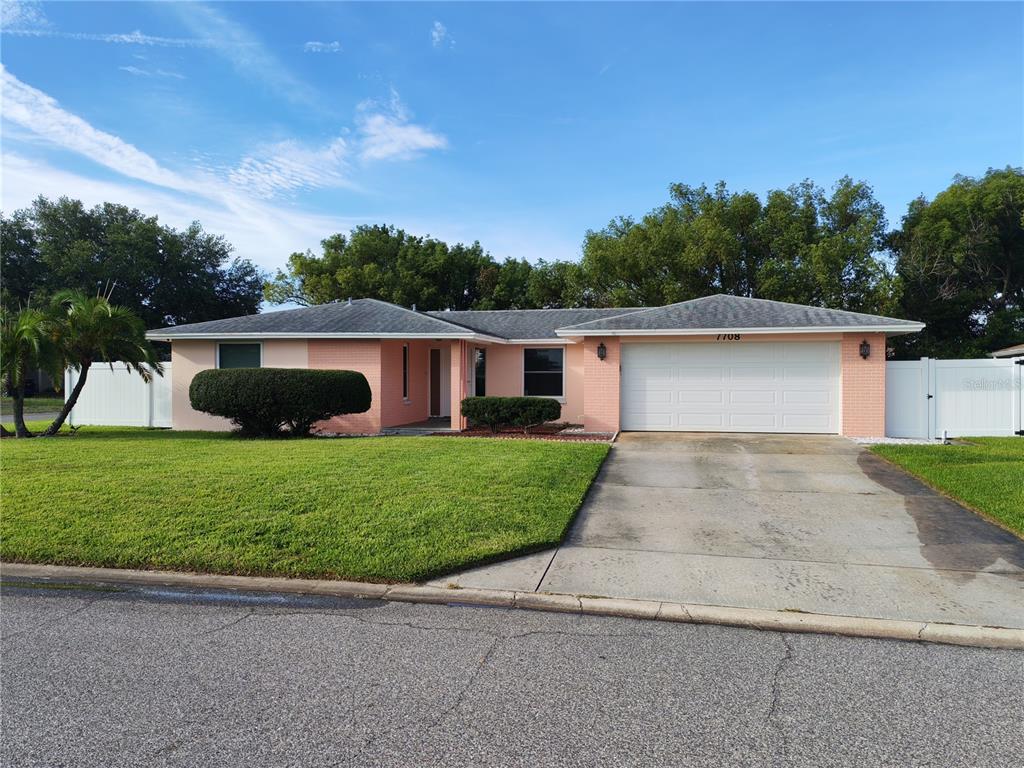 A single-story house features a pink brick exterior, a recessed entryway, and manicured landscaping — 7708 ROSEWOOD DRIVE, PORT RICHEY, FL