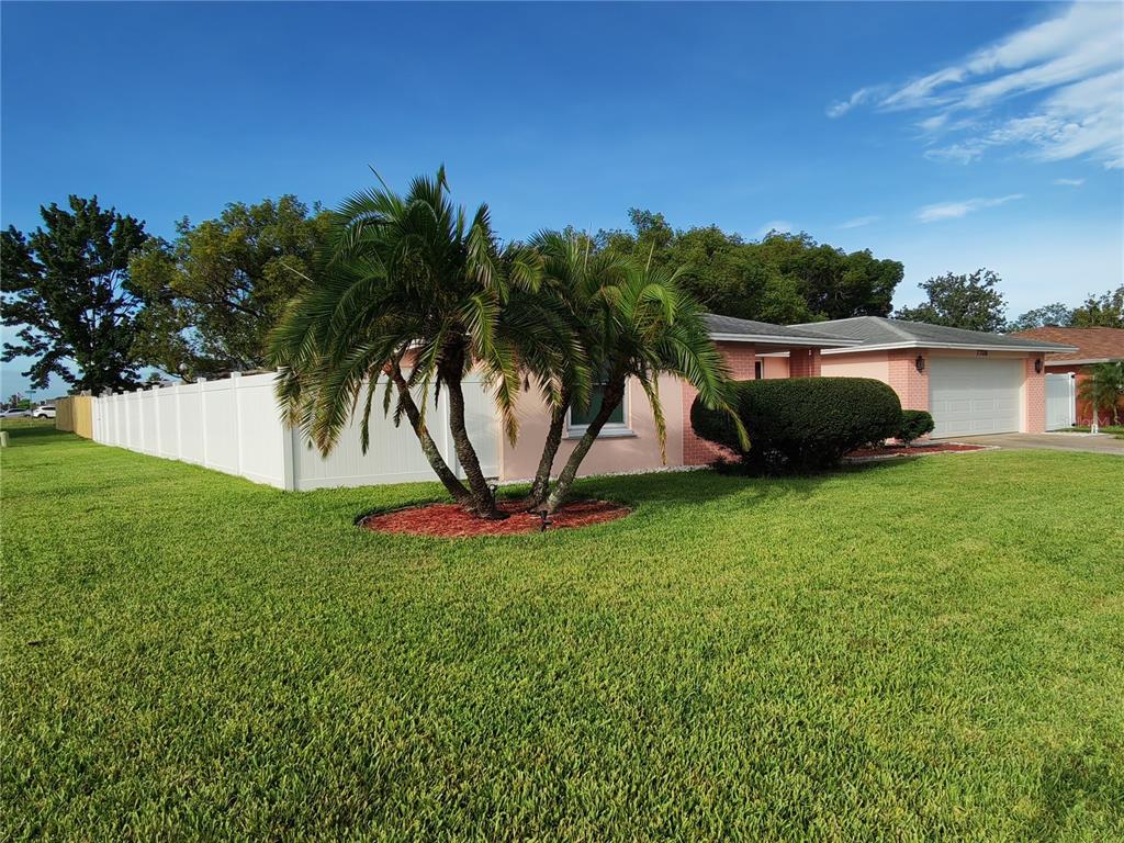 A peach-colored house exterior features a brick pillar, a stone-tiled porch, and a front door — 7708 ROSEWOOD DRIVE, PORT RICHEY, FL
