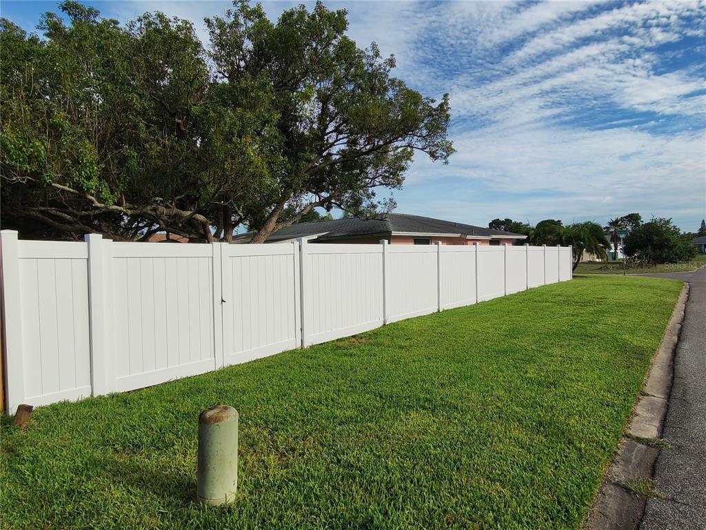 A covered brick porch features stone flooring, a small garden bed, and a view of landscaping — 7708 ROSEWOOD DRIVE, PORT RICHEY, FL