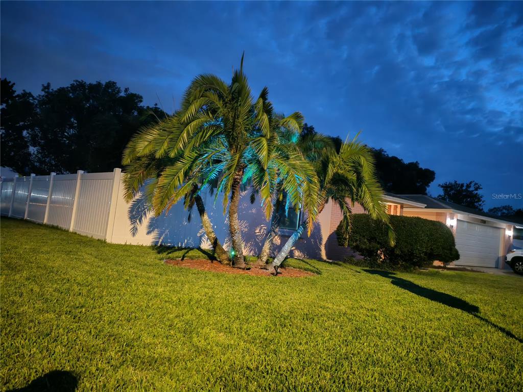 A pink house with a white fence and palm trees sits on a green lawn — 7708 ROSEWOOD DRIVE, PORT RICHEY, FL