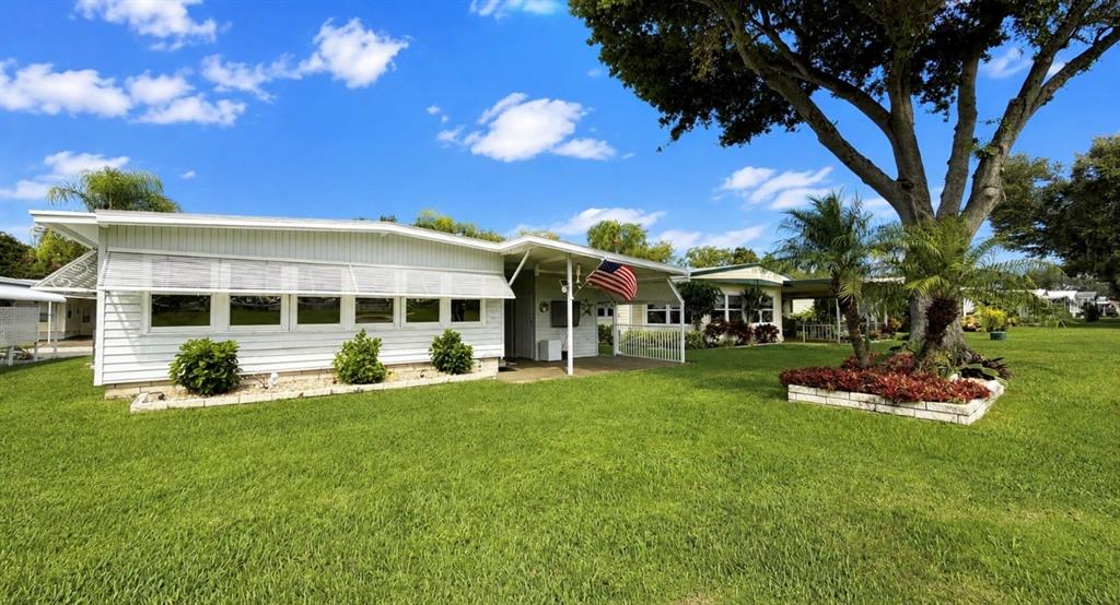 A white single-story manufactured home with a covered porch and an American flag — 1100 BELCHER ROAD S UNIT 448, LARGO, FL
