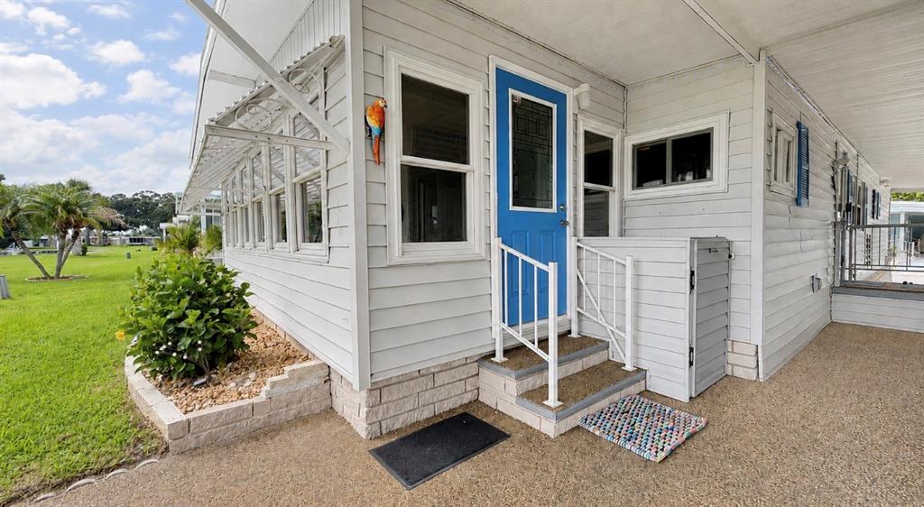 A light gray mobile home exterior features a bright blue front door and white railings — 1100 BELCHER ROAD S UNIT 448, LARGO, FL