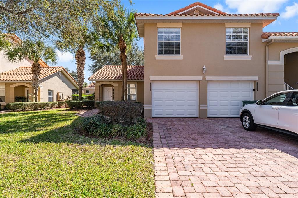 A two-story house with a two-car garage, a brick paver driveway, and palm trees — 5427 COMPASS POINT UNIT 1, OXFORD, FL