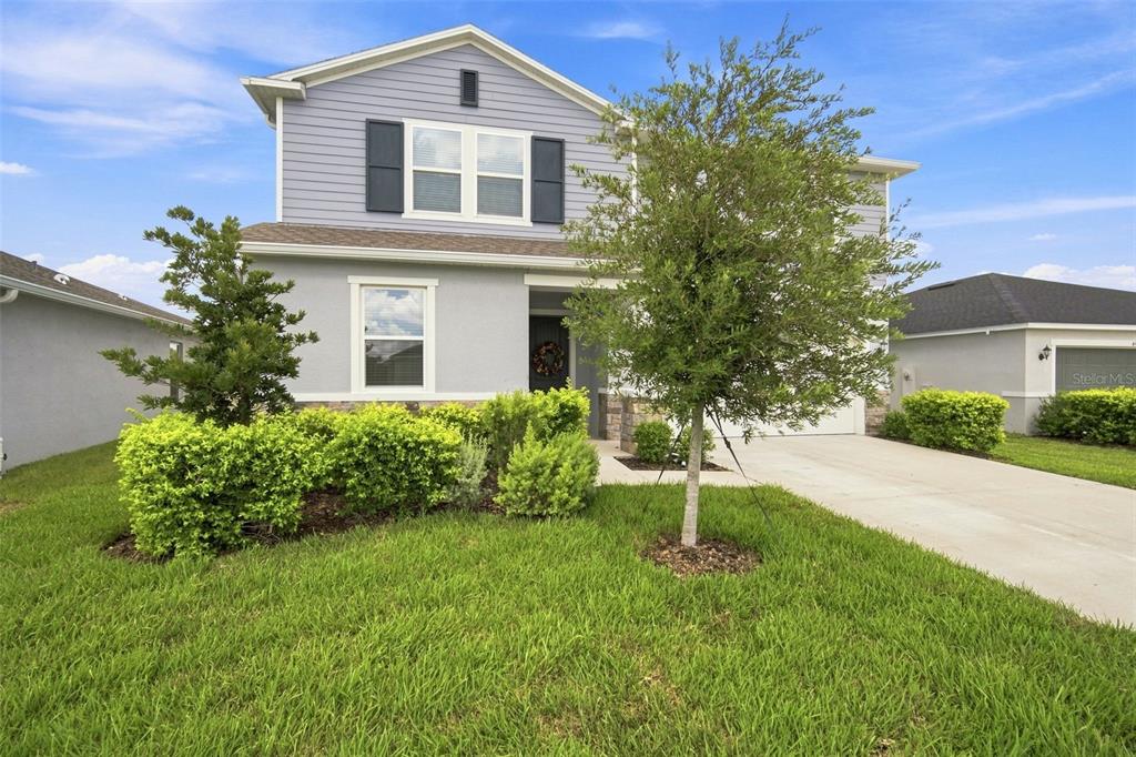 A two-story house with light blue siding, a concrete driveway, and a manicured front lawn — 6473 BURNING OPAL BEND, LAND O LAKES, FL