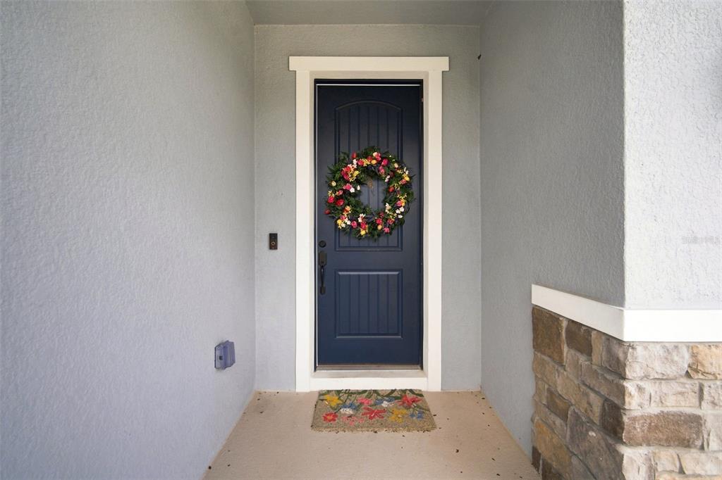 A dark blue front door with a floral wreath sits under a covered entryway — 6473 BURNING OPAL BEND, LAND O LAKES, FL