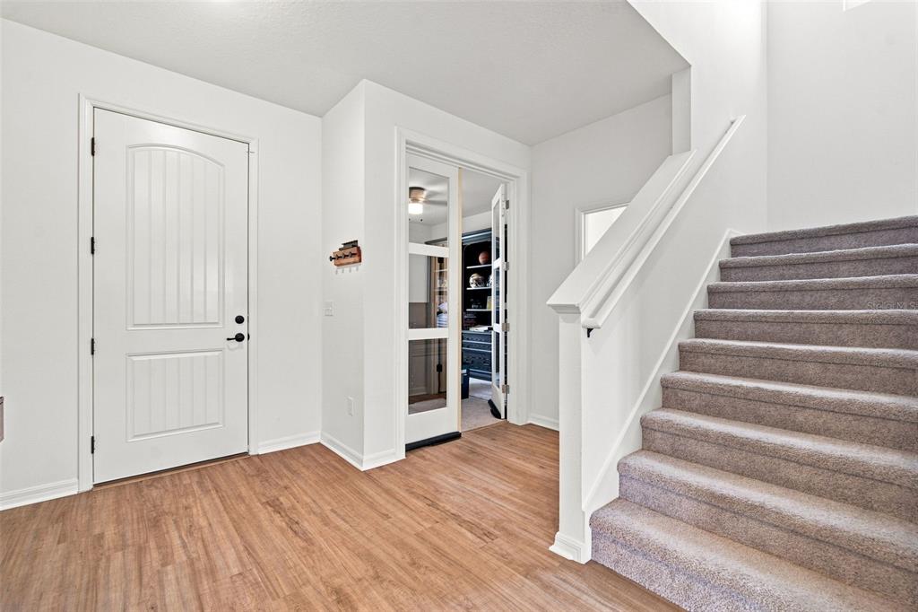 An entryway features wood-look flooring, a white front door, French doors, and carpeted stairs — 6473 BURNING OPAL BEND, LAND O LAKES, FL