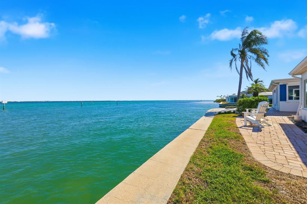 A waterfront patio with a concrete seawall, lawn, and two chairs beside a house — 957 SPANISH DRIVE N, LONGBOAT KEY, FL