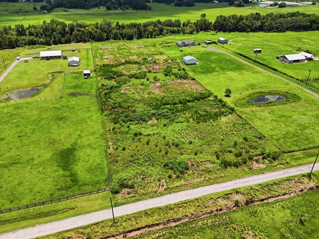 An aerial view shows a rectangular, overgrown lot situated between two fenced pastures with outbuildings — 737 BROOKE ROAD, FORT MEADE, FL