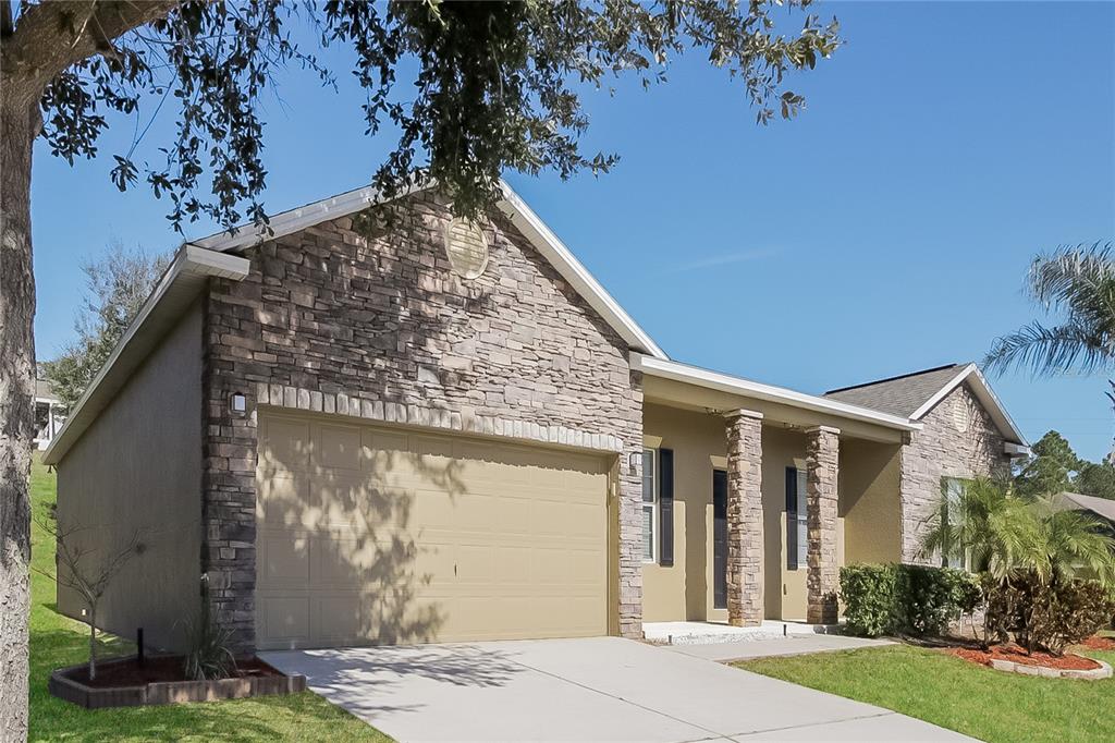 A single-story house with a stone facade, tan garage door, and a covered front porch — 1117 SPRUCE RIDGE COURT, MINNEOLA, FL