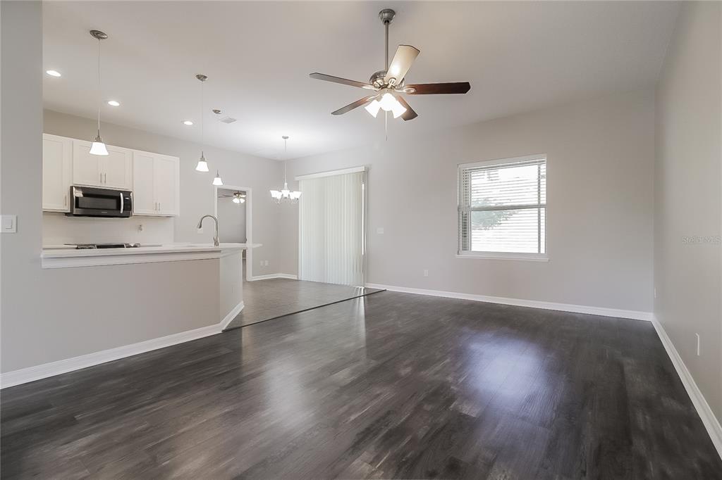 An open-concept living area features dark wood-look flooring, a ceiling fan, and a kitchen island — 1117 SPRUCE RIDGE COURT, MINNEOLA, FL
