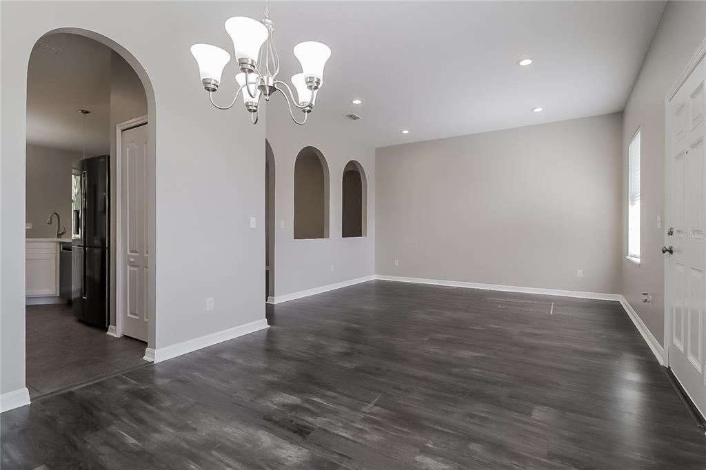 A dining room with dark wood-look flooring, an arched entryway, and a modern chandelier — 1117 SPRUCE RIDGE COURT, MINNEOLA, FL