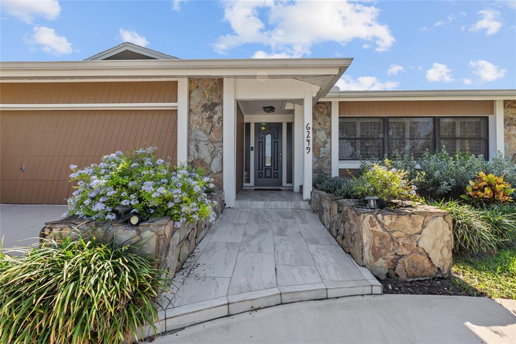 The exterior of a single-story house features a stone facade, a tiled walkway, and landscaping — 6249 HILLSIDE AVENUE, SEMINOLE, FL