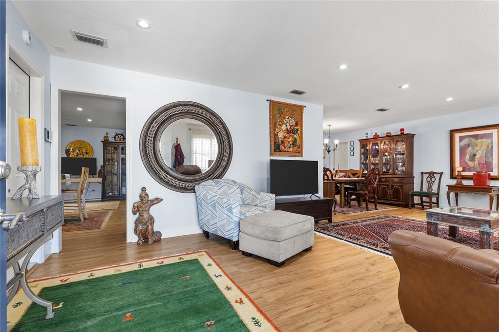 A living room with light wood floors, a large round mirror, and a green rug — 6249 HILLSIDE AVENUE, SEMINOLE, FL