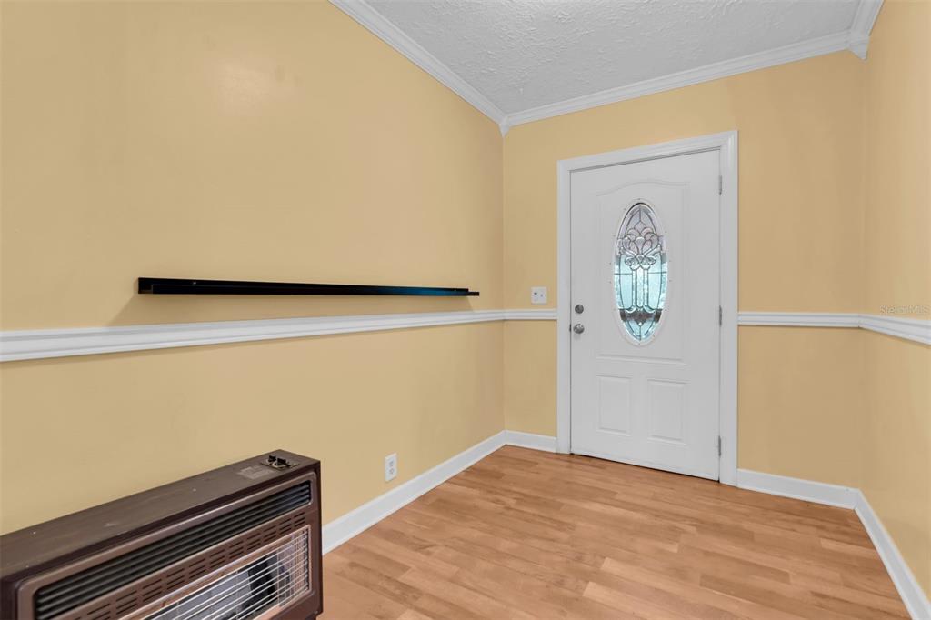 An entryway features light yellow walls, wood-look flooring, a white front door, and a wall heater — 7224 SHAW RD., BROOKSVILLE, FL