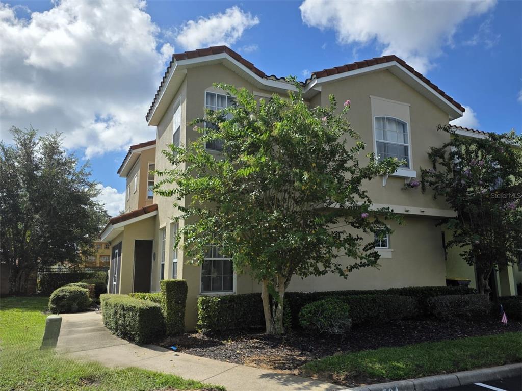 A two-story tan stucco townhouse with a tile roof and a small front garden — 734 MONROE CIRCLE, DAVENPORT, FL
