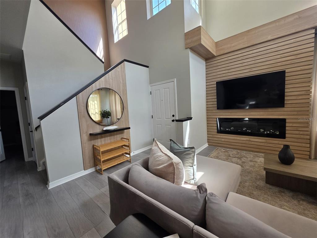 A living room features a wood-paneled accent wall with a fireplace, television, and staircase — 734 MONROE CIRCLE, DAVENPORT, FL