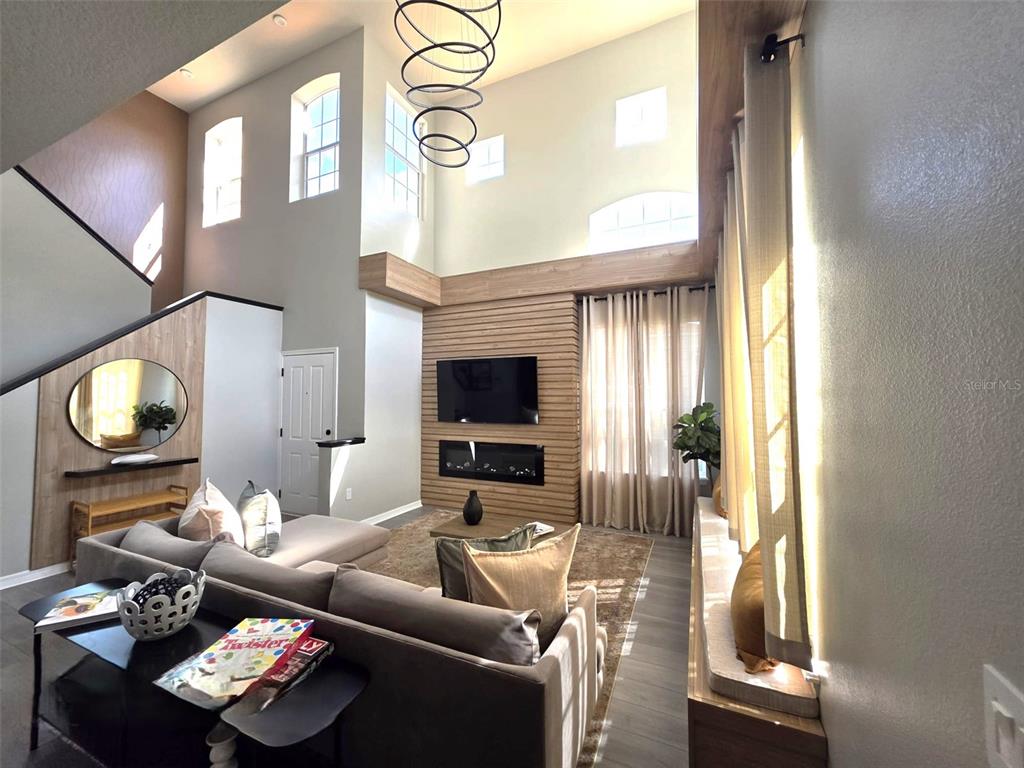 A living room features a two-story ceiling, wood-paneled accent wall, fireplace, and sectional sofa — 734 MONROE CIRCLE, DAVENPORT, FL