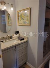 A bathroom features a gray vanity with a stone countertop, a mirror, and wall lighting — 1370 GREENWAY DRIVE, MOUNT DORA, FL