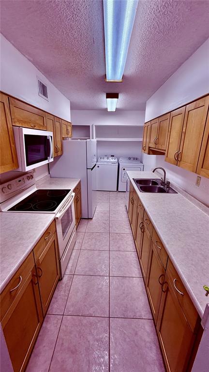 A kitchen with light wood cabinets, white countertops, tile flooring, and an adjacent laundry area — 6519 W NEWBERRY ROAD UNIT 912, GAINESVILLE, FL